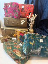 Load image into Gallery viewer, A collection of colorful, patterned zippered pouches made from vintage tapestry fabrics, styled with antique suitcases, a small decorative chest, and dried grass in a vase.